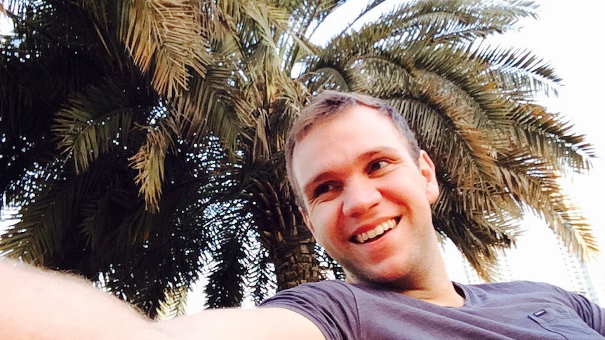 A smiling man taking a selfie in front of a palm tree.