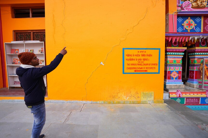 A man points at a wall with a crack in it. 