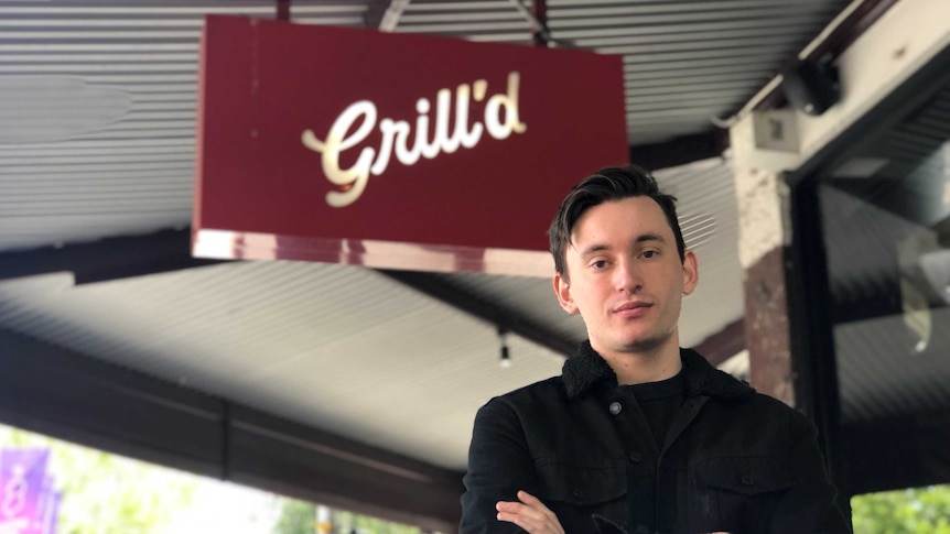 Patrick Stephenson, a man in black, stands in front of a Grill'd burger store.