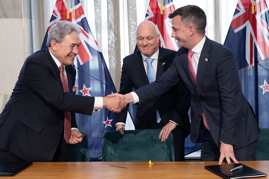 Two men shake hands while the other man looks happy but nervous. 