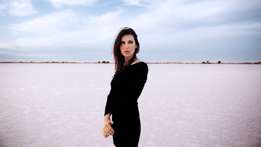 Adalita wears a black dress and stands in the middle of a desert