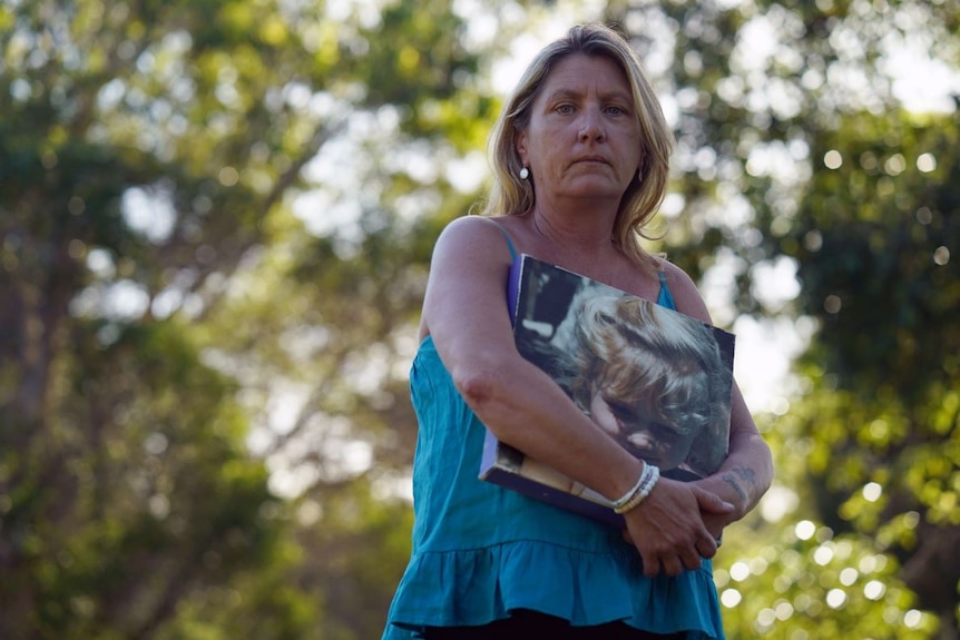 A woman with a serious facial expression holds a large canvas photograph of her young daugther