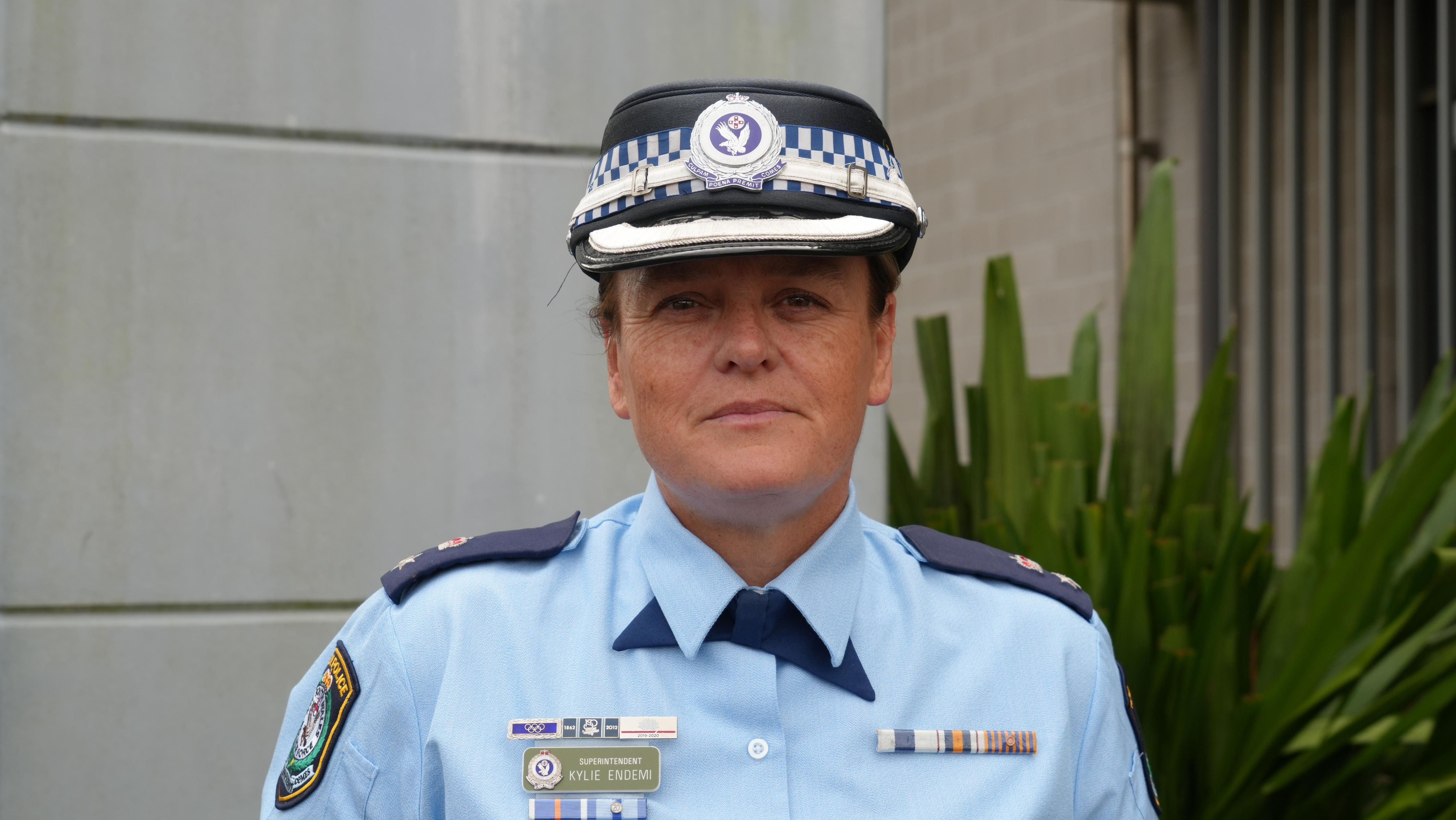 A policewoman in uniform and a police hat looking at the camera.