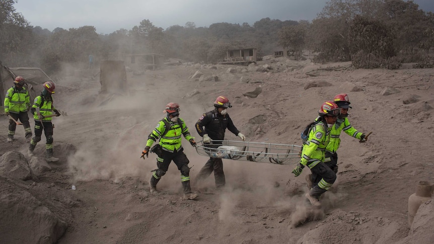 Rescue workers run for cover near Volcan de Fuego. The area is covered in piles of thick grey ash.