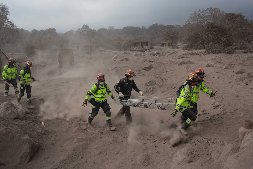 Rescue workers run for cover near Volcan de Fuego. The area is covered in piles of thick grey ash.