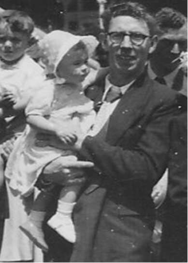 Anne Connor is a toddler wearing a white bonnet, her dad Jock holds her and wears a suit jacket