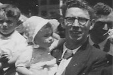 Anne Connor is a toddler wearing a white bonnet, her dad Jock holds her and wears a suit jacket