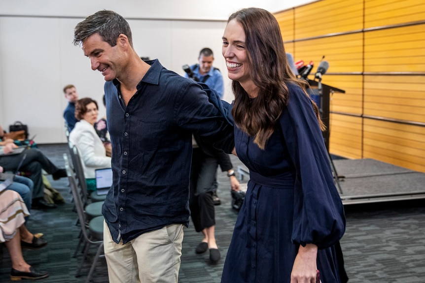 Jacinda Ardern is pictured walking away from a press conference with her partner Clarke Gayford. They are smiling.
