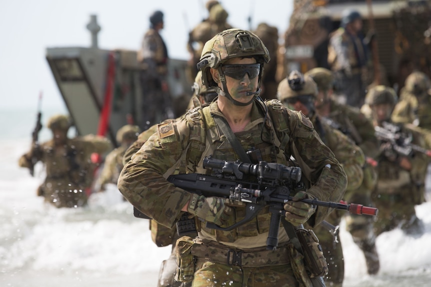 Soldiers dressed in camo holding guns on the beach.