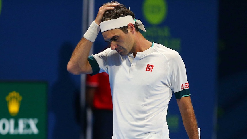 A headband-wearing tennis player looks down and puts his hand to his head during a match.