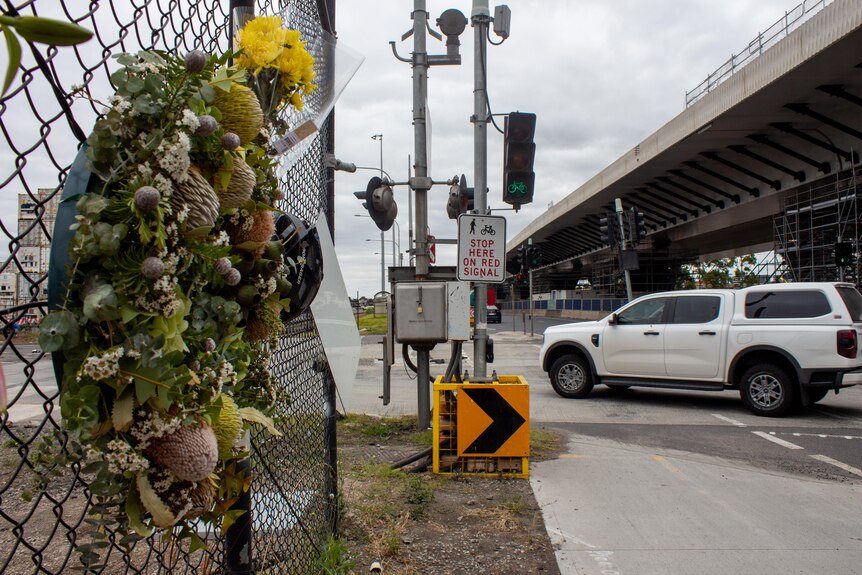 A wreath of flowers on a fence, ahead is a bike path with green light and a car turning left across the path