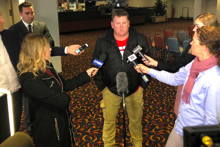 Former miner Simon Turner surrounded by journalists with microphones at a bowling  club in Beresfield near Newcastle.