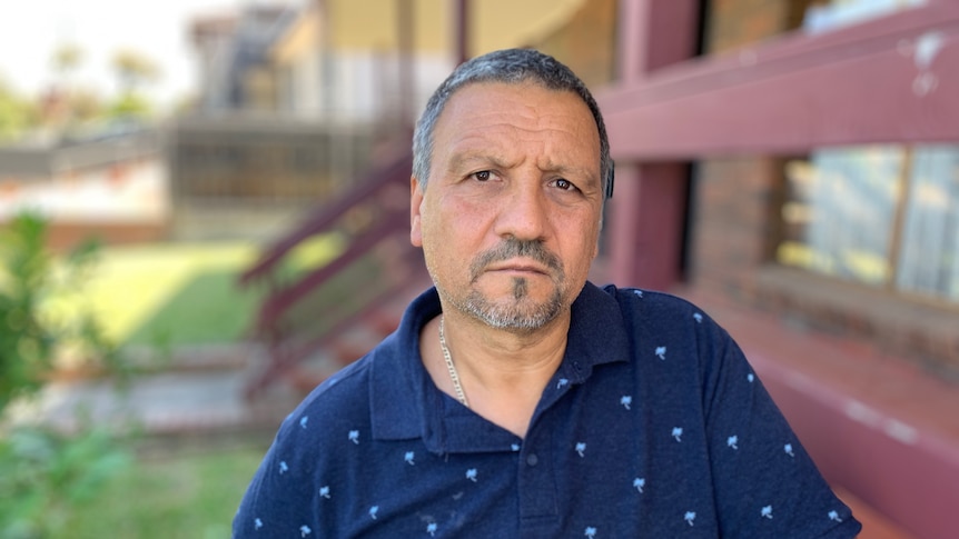 A profile of a man with dark hair wearing a short-sleeve blue button-up shirt.