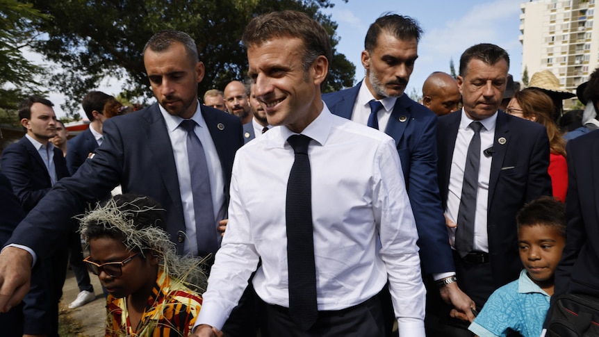 Macron holds hand with young boy who is wearing sunglasses and who looks like a rockstar