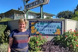 A smiling woman stands outside a caravan park sign that says 'Newmarket gardens'