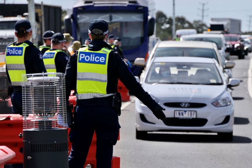 A group of police stand on a freeway. Cars are lined up into the distance. One officer directs traffic.