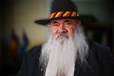 A man with a beard and a hat with the colours of the Aboriginal flag on its band.