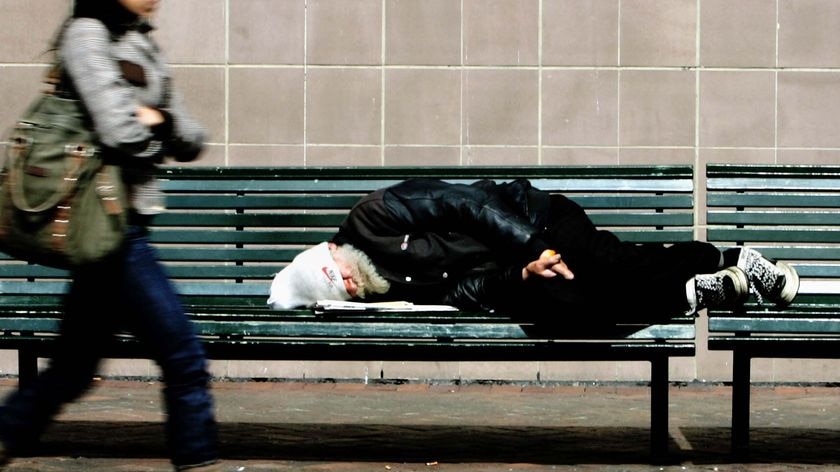 A homeless man sleeps on a bench in Sydney street