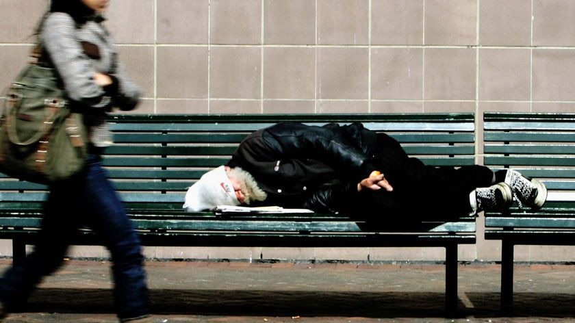 A homeless man sleeps on a bench.