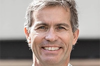 Peter Hoj smiles in a headshot. He is wearing a grey pinstripe suit, a white shirt and orange polka dot tie.