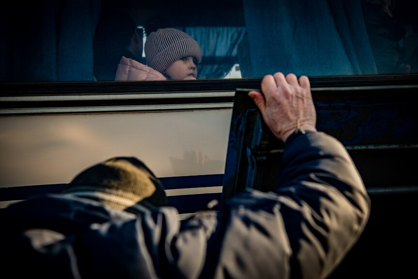 A child in a beanie looks out the window of a bus, seen from the outside 