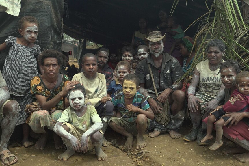 A large family, some with paint decorating their bodies, crouch in front of an erected tarpaulin