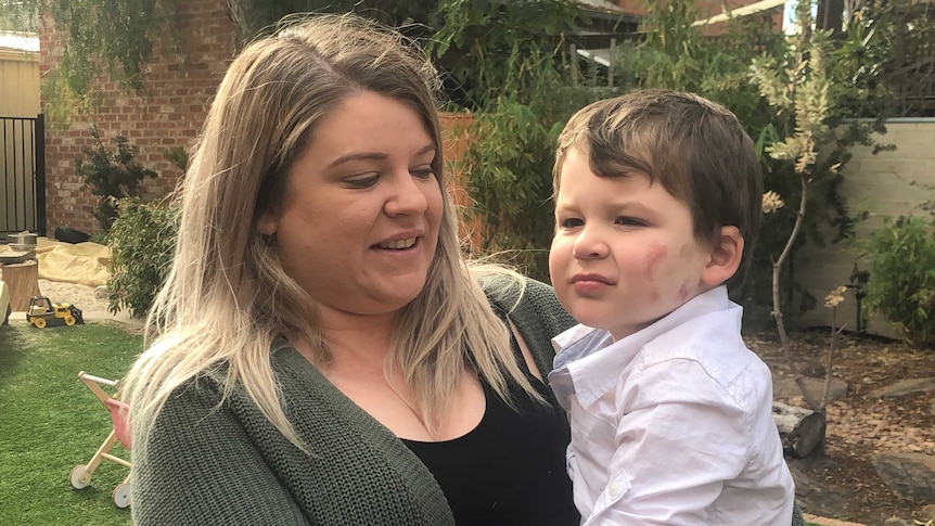 A mother stands holding her son who has lost limbs through meningococcal B