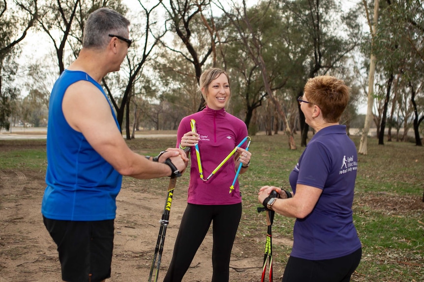 Jacinta talks and laughs with two others, holding walking poles.