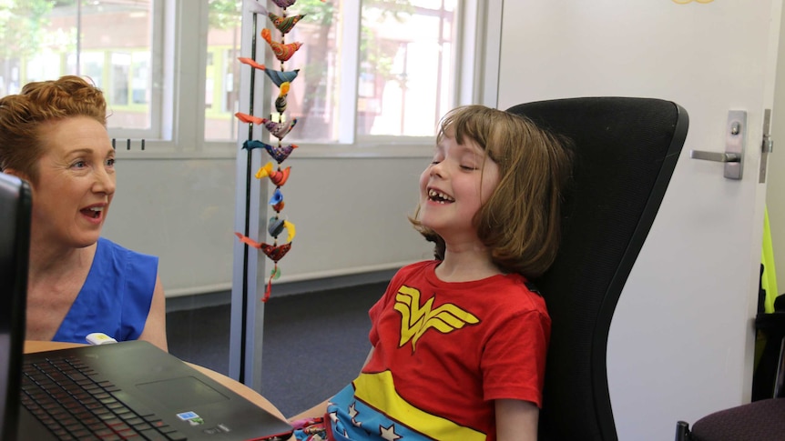 A young girl laughs while looking at a laptop.