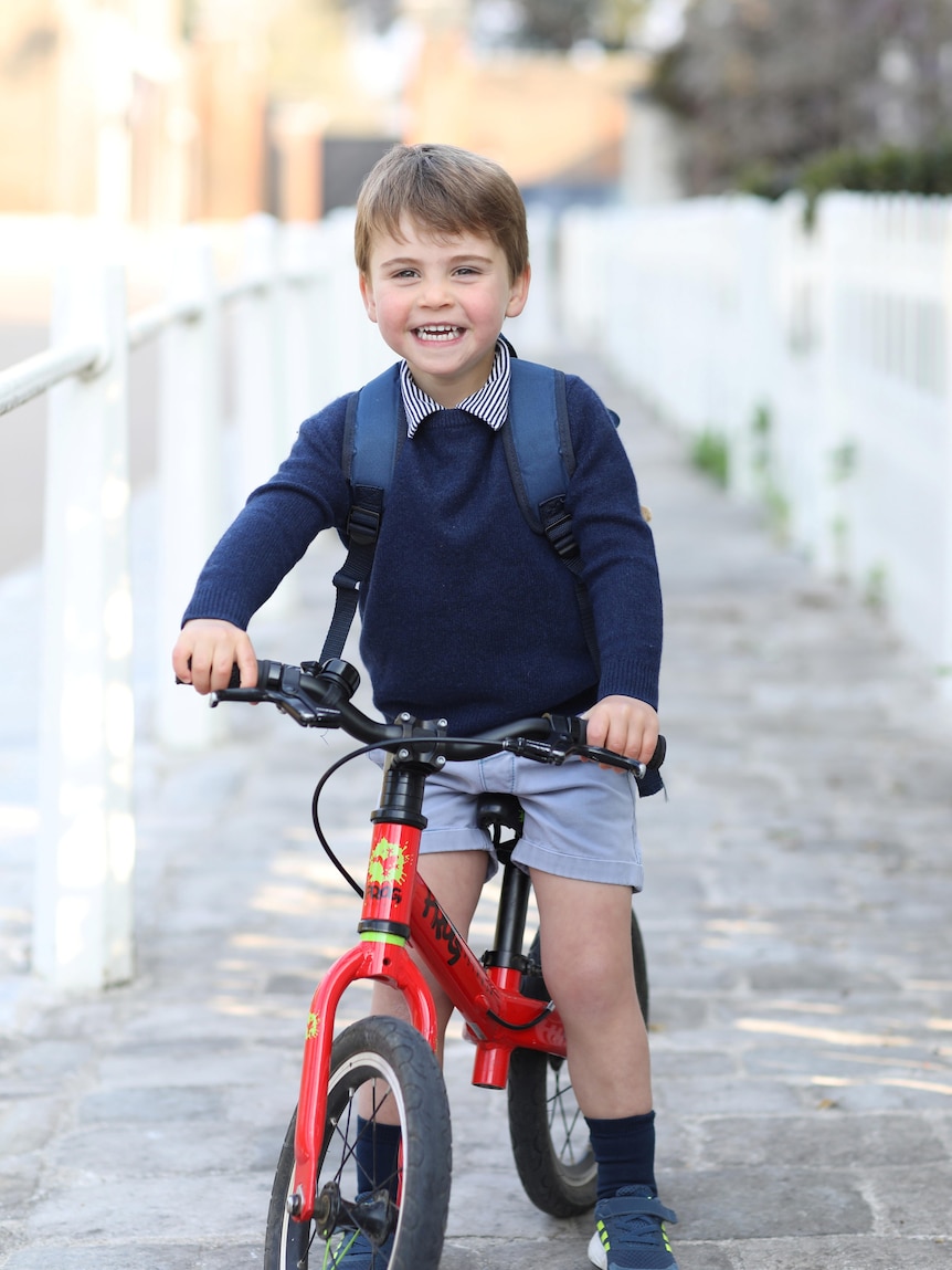 Britain's Prince Louis smiles on a red bicycle 