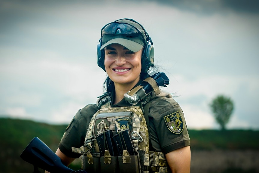 A young woman in combat gear smiles 