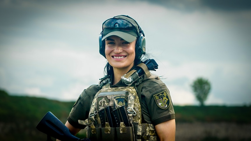 A young woman in combat gear smiles 