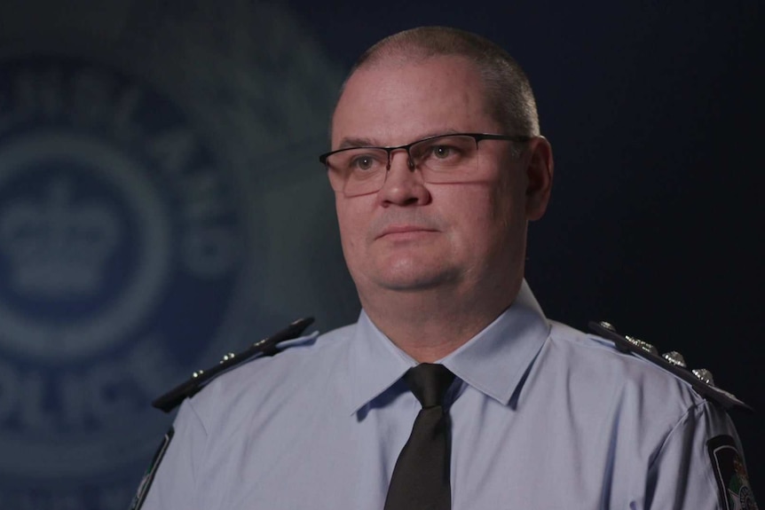 MCU of Chief Superintendent Tony Fleming sitting in front of a large soft focus Qld Police logo