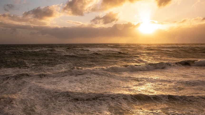 The sun sets over a stormy ocean with a surfer amidst it all