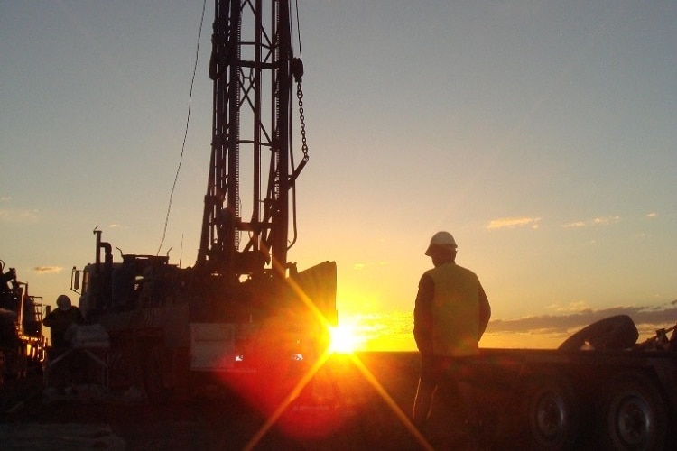 Sun set over a drilling rig with a worker standing in the foreground.