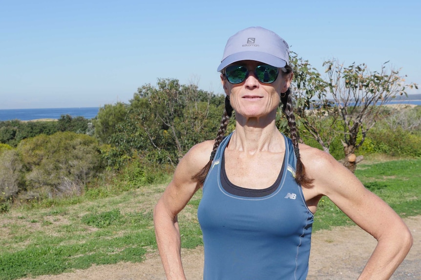 A woman in running gear standing on a headland looks at the camera.