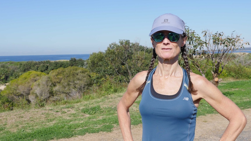 A woman in running gear standing on a headland looks at the camera.