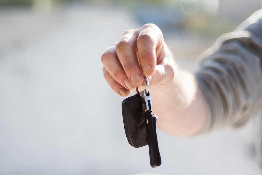 A hand holds out a key ring with a car key on it.