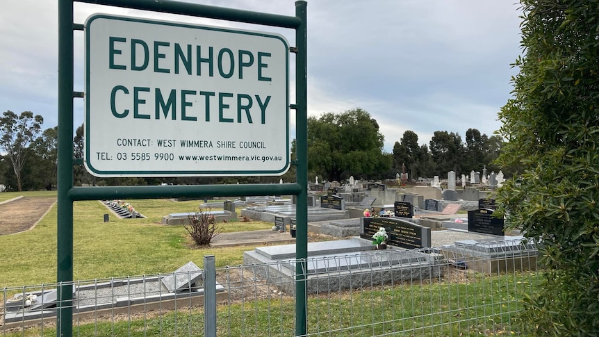 A green and white metal sign with the words Edenhope cemetery stands in front of a graveyard 
