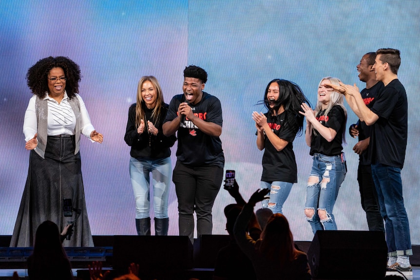 Oprah Winfrey and cast of Cheer on a stage, smiling.