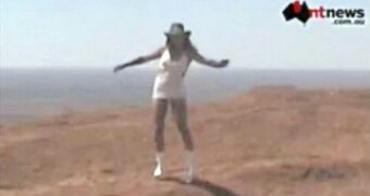 Woman in a white dress and akubra stands on top of Uluru