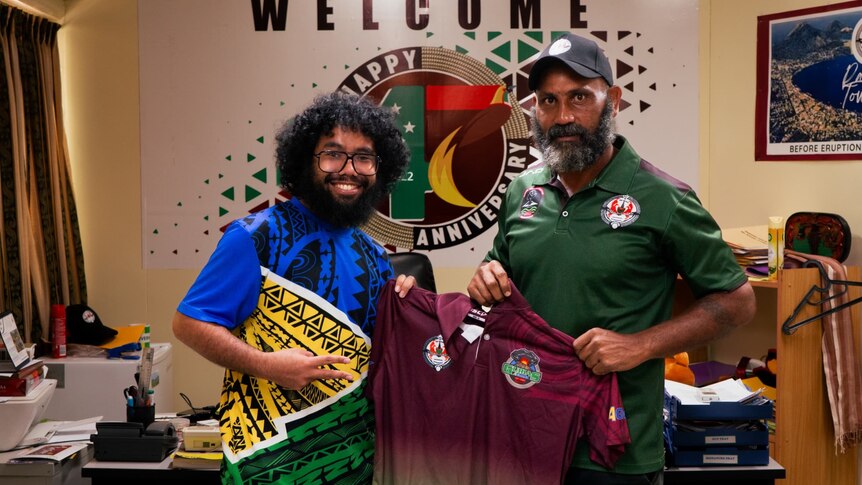 A reporter and the governor stand smiling in an office holding a PNG kumuls rugby jersey