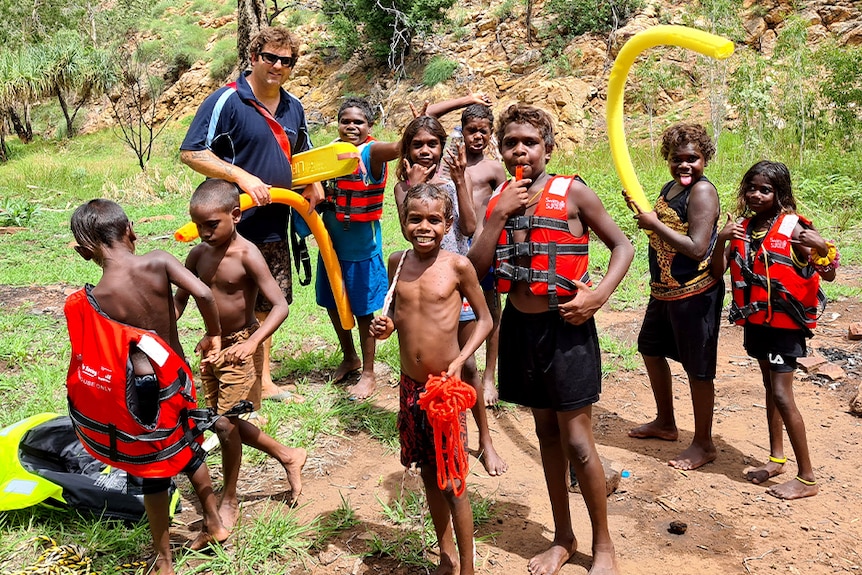 A group of children wearing life jackets stands by a river near Warmun.