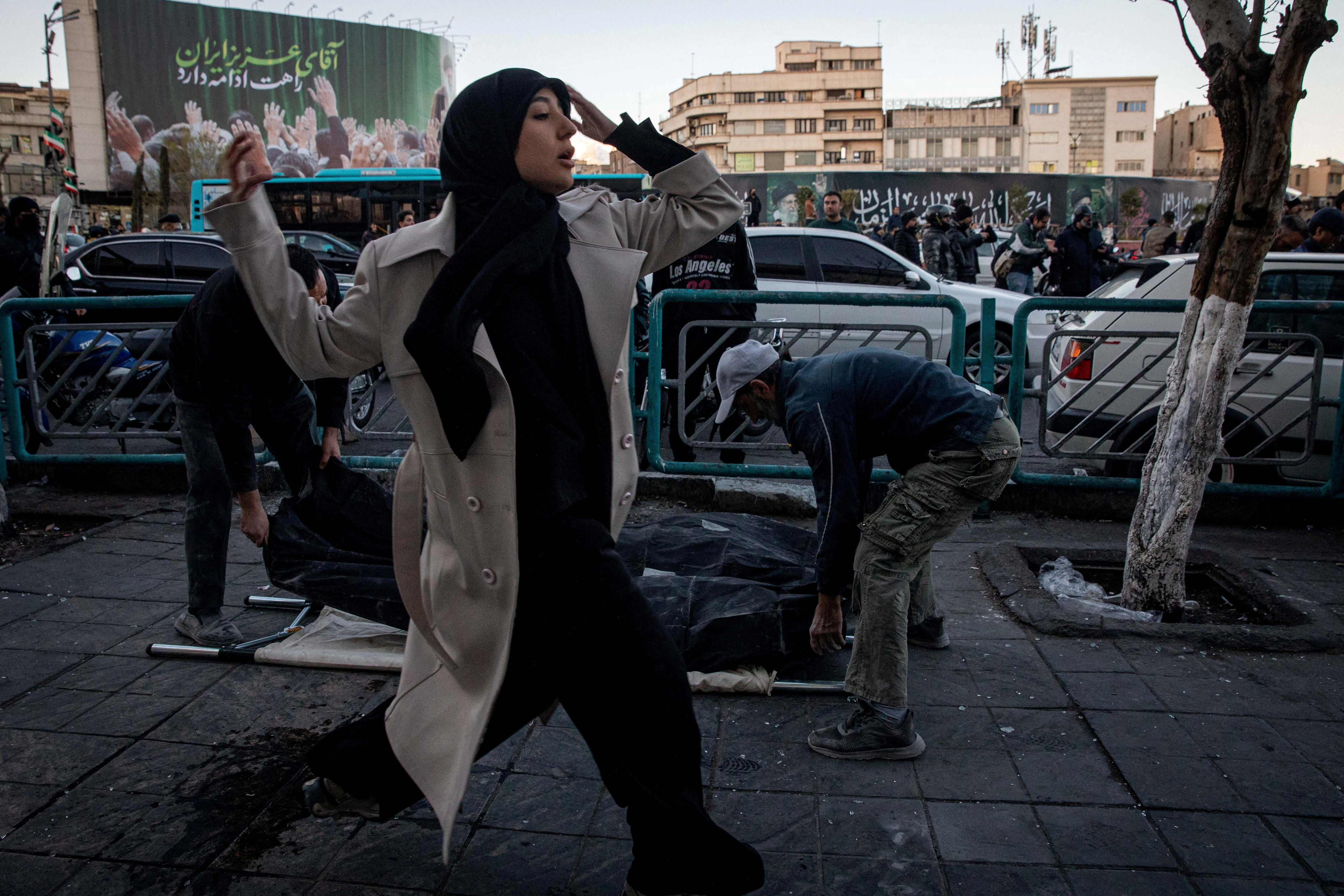 A woman runs past people placing casualties of an Israel and US strike on a police station in Tehran, Iran March 3, 2026.