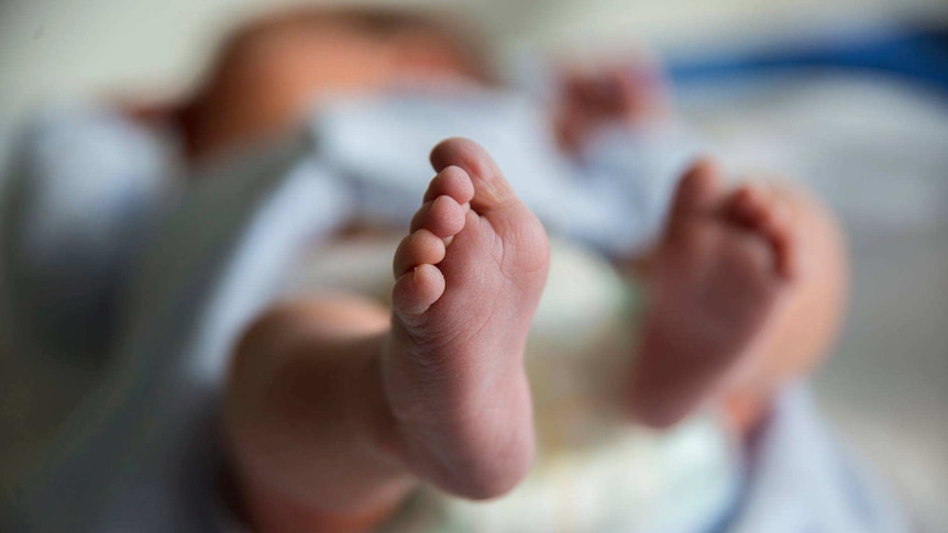 A newborn baby is shown lying down, with one of its feet in the foreground of the image.