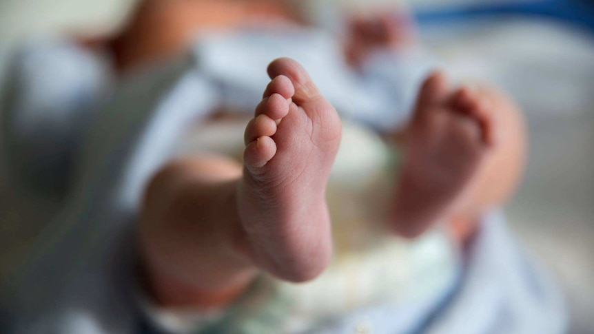 A newborn baby is shown lying down, with one of its feet in the foreground of the image.