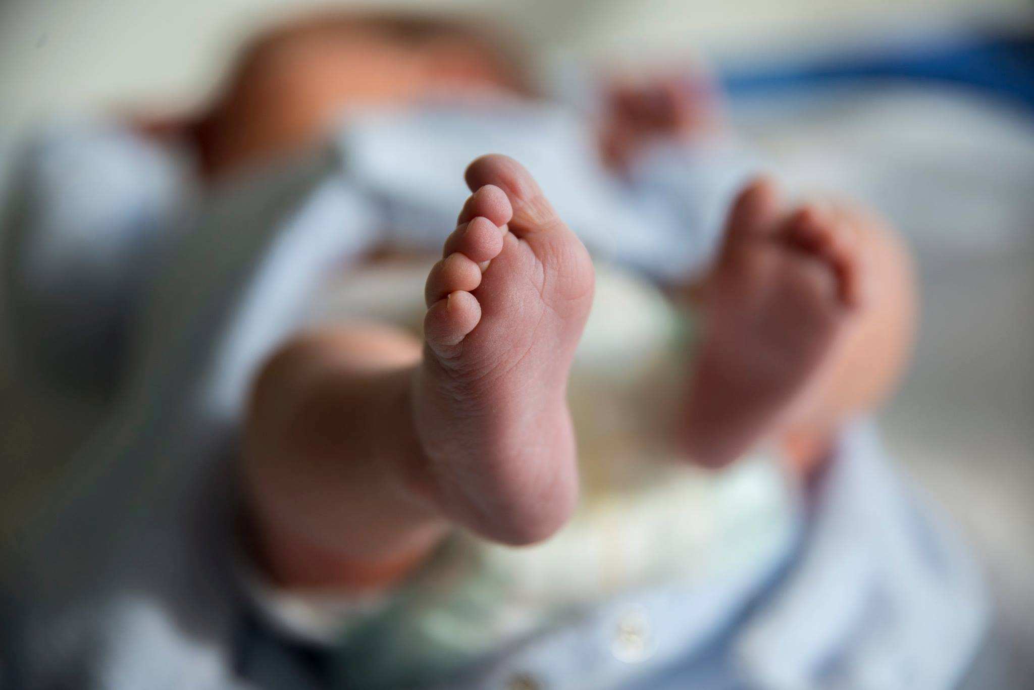 A newborn baby lying down, with one of its feet in the foreground of the image.