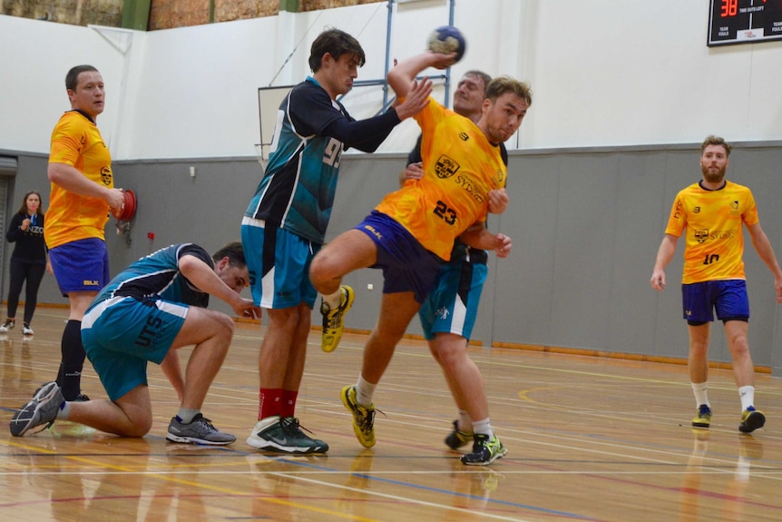 A Sydney Uni handball player jumps and throws the ball as opponents try and stop him.
