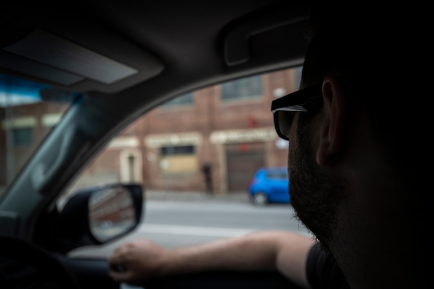 A man sits in a car watching a building.