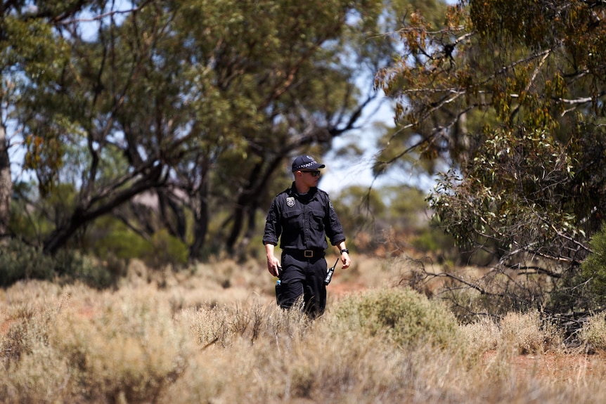 A police officer walks through scrub